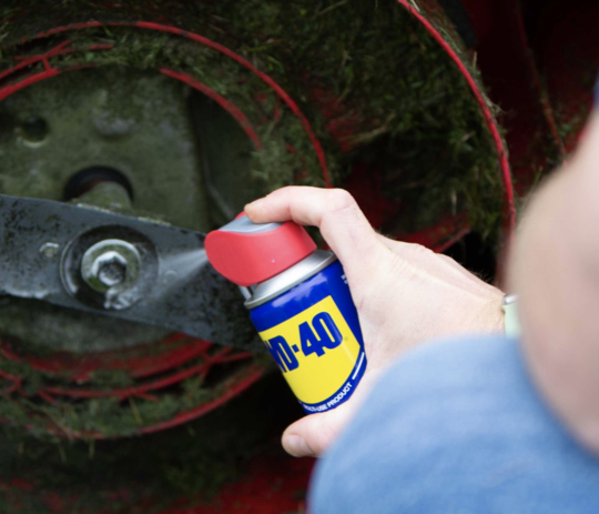 man applying can of WD-40 product to lawnmower blade